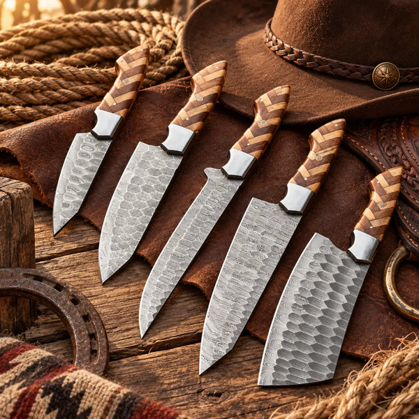 5 hammered Damascus kitchen knives and a cleaver with patterned wooden handles arranged on a rustic wooden surface next to a leather hat and rope