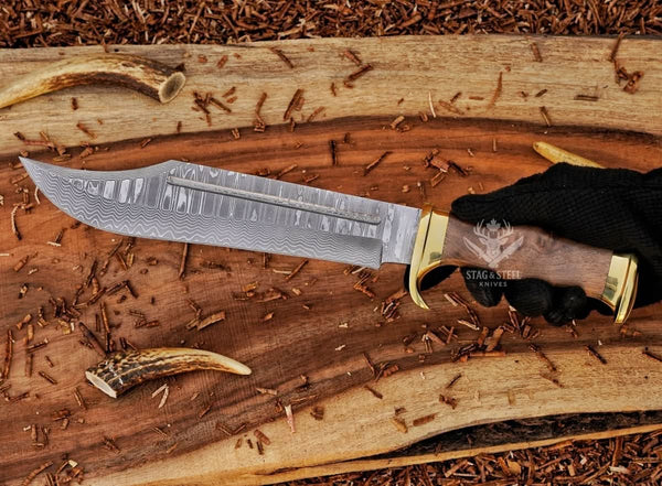 Damascus bowie knife with walnut handle and brass guard held in hand
