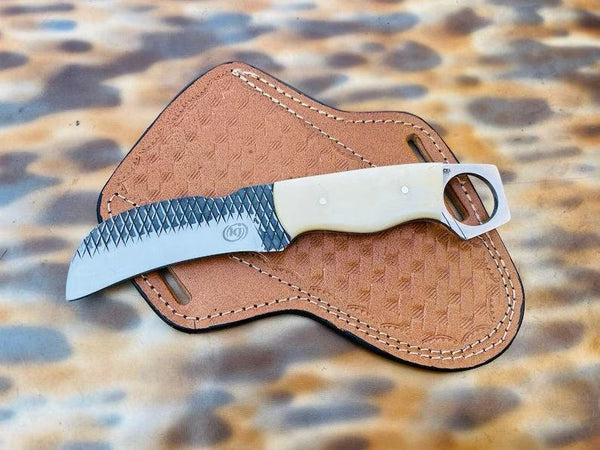 A fixed-blade knife with a textured silver blade and cream handle, resting on a brown leather sheath over a leopard-print surface.