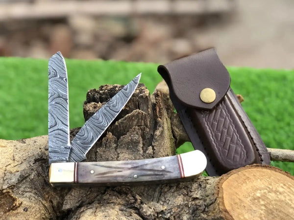 Two pocket knives with leather sheaths on a wooden stump with a blurred natural background.