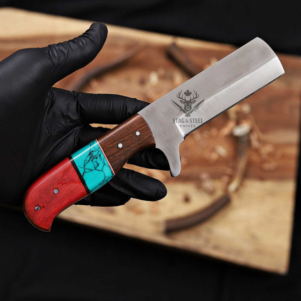 Knife with a wooden handle featuring red, turquoise, and brown colors, held by a gloved hand against a blurred background.