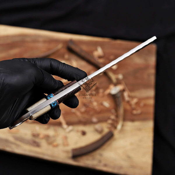 Hand holding a knife with 'Stag & Steel Knives' branding on a wooden surface.