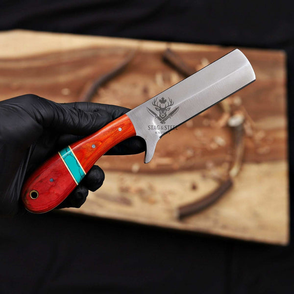 Knife with a red handle and visible brand logo held by a gloved hand on a wooden background.