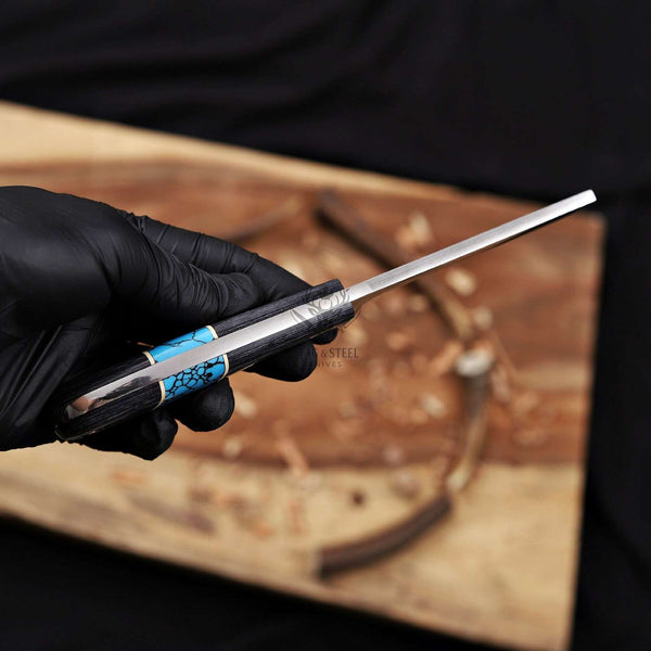 Hand holding a knife with a black and blue handle over a wooden surface.