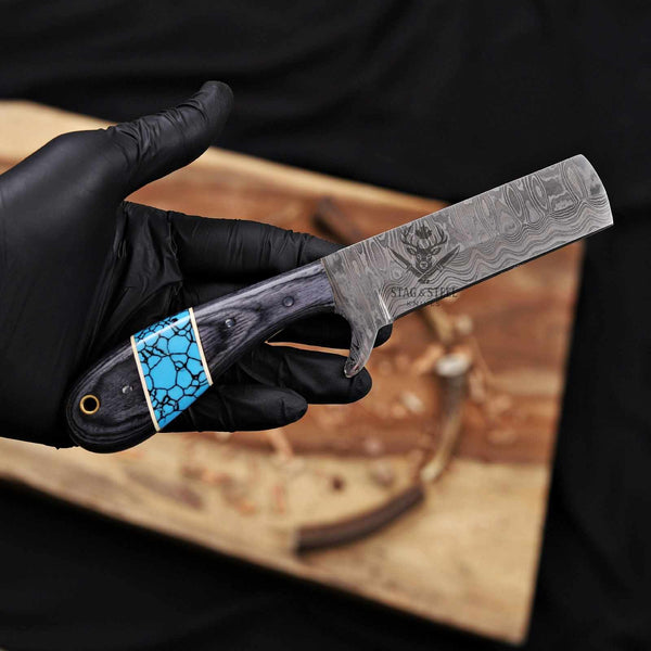 Hand holding a Damascus steel knife with a blue inlay on a wooden surface.