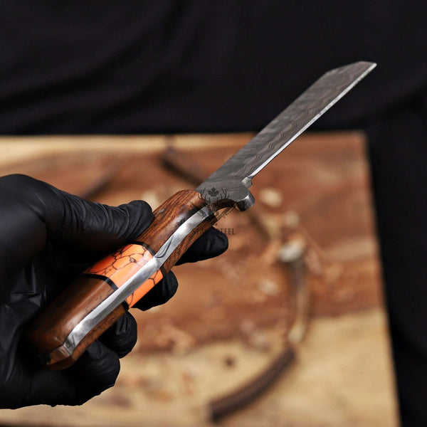 Hand holding a folding knife with wooden handle and metal blade on a wooden surface.