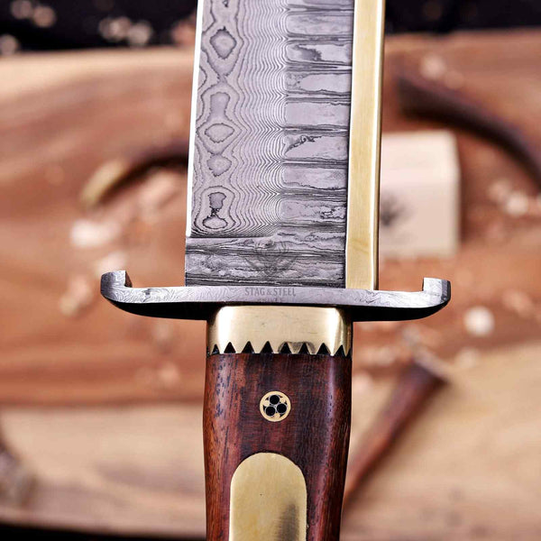 Macro of Damascus guard and sawtooth brass bolster on Iron Mistress bowie knife