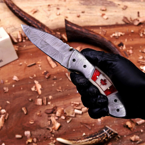 Folding pocket knife with handmade Canada flag handle and Damascus steel blade in hand