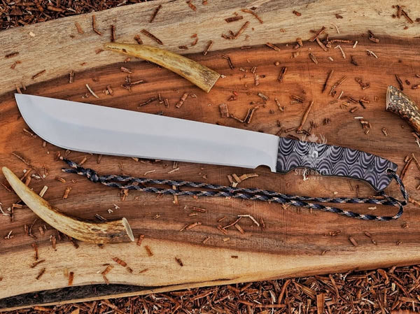 Full tang D2 steel machete knife with Grey Micarta handle, satin blade, and paracord on rustic wood
