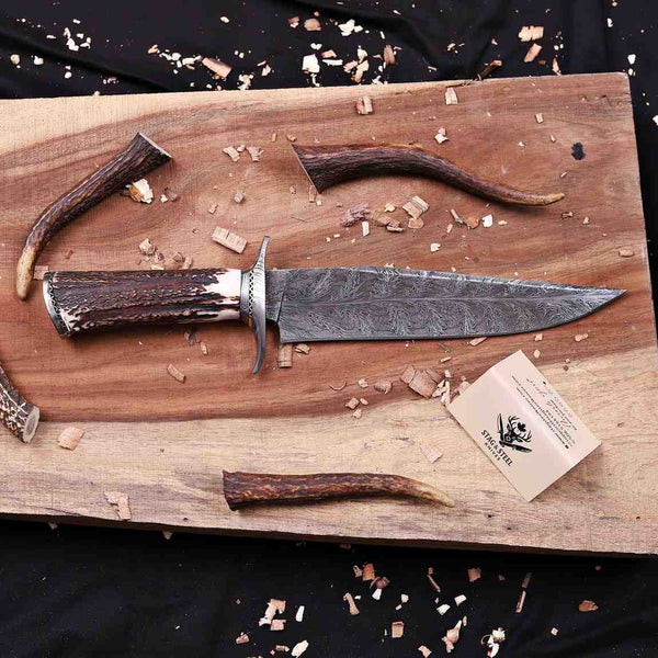 Full profile of handmade Feather Damascus bowie knife with antler handle and wood shavings