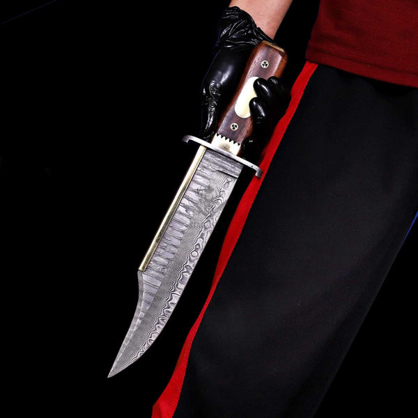 Iron Mistress Damascus bowie knife with brass spine held against black background