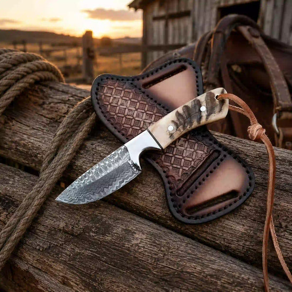 A fixed-blade knife with a patterned steel blade and a carved bone handle rests on a leather sheath, placed on weathered wooden logs outdoors at sunset.