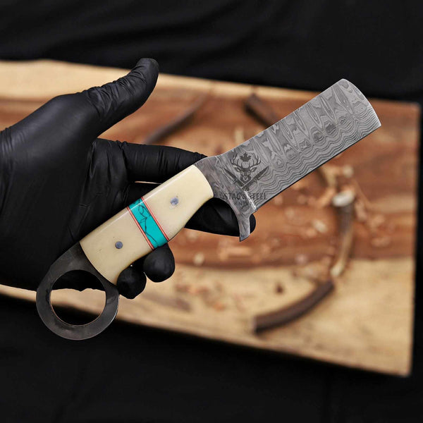 Hand holding a Damascus knife with a decorative handle against a dark background