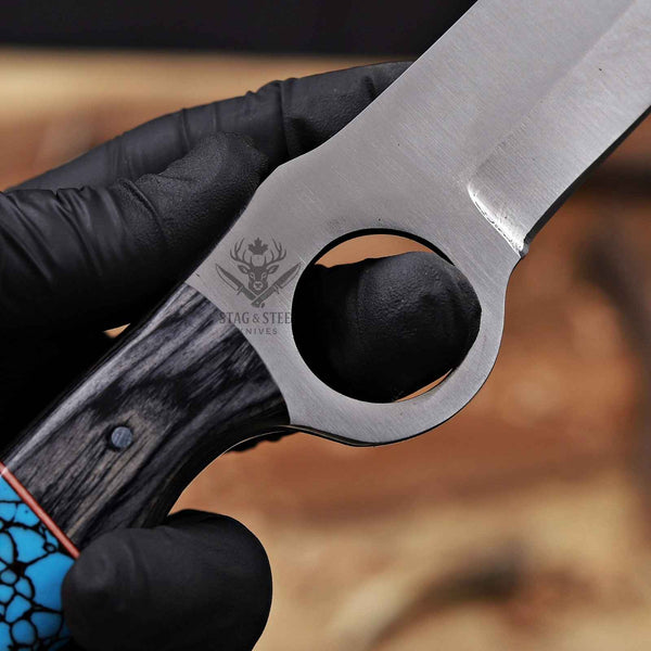 Close-up of a knife with a black handle and metal blade, held by a gloved hand.