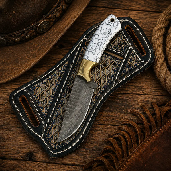 Cowboy Damascus knife with white crackle-pattern handle and decorative leather sheath on a rustic Western background
