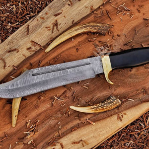 Damascus bowie knife with black handle and brass guard on rustic wood slab