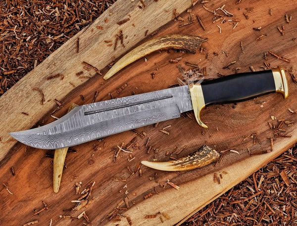 Damascus bowie knife with black handle and brass guard on rustic wood slab