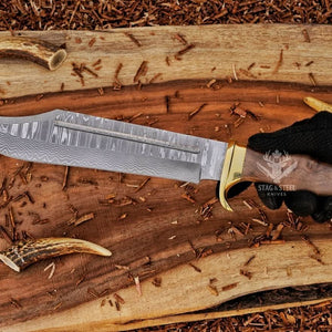 Damascus bowie knife with walnut handle and brass guard held in hand