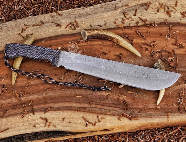 Damascus machete with layered G10 handle and paracord lanyard on rustic wood