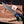 A hand wearing a black glove holds a San Mai Damascus Finger Guard Bowie knife over a wooden cutting board with wood shavings and a small branded card. The knife has a Stainless San Mai Damascus steel blade and a colorful handle with blue, green, and gold marbled sections.