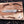 A custom handcrafted hunting knife with a Damascus steel blade and a dark wood handle, displayed on a wooden cutting board with antlers, wood shavings, and a brand card.