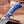 A close-up of a custom knife with a blue marbled resin handle and a Damascus steel blade, set against a blurred workshop background.