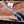A hand wearing a black glove holds a fixed-blade knife with a patterned steel blade and a blue marbled handle over a wooden cutting board with wood shavings and antlers.
