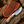 Handmade rasp steel gut hook hunting knife with a pine cone resin handle and an etched mountain pattern, resting beside a tooled leather sheath on rustic wood.