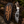 A fixed-blade knife with a patterned steel blade and a stag emblem on its handle, displayed beside a dark leather sheath featuring a carved stag and American flag design, set on a rustic log with moss and pine branches.