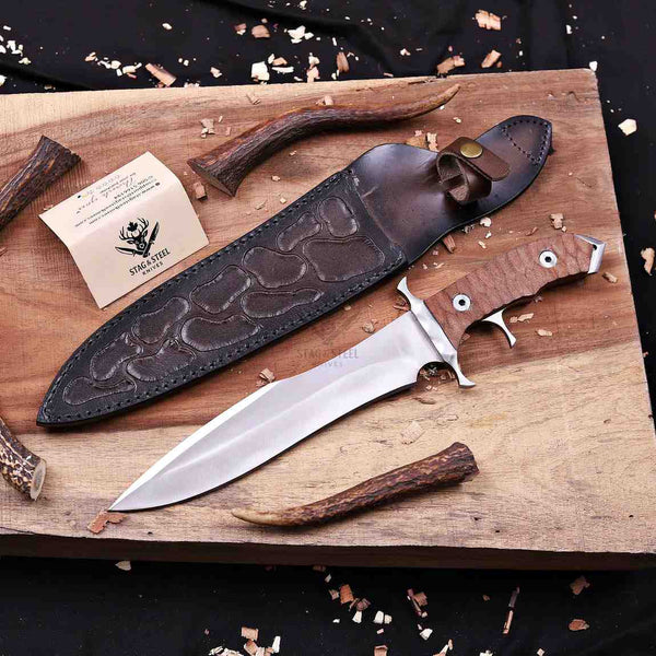 Fixed-blade steel knife with a brown wood handle and embossed dark brown leather sheath, displayed on a wooden board with stag antlers