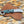 A custom folding pocket knife with a marbled green and blue handle, a silver studded blade, and a silver ring pommel, resting on its brown woven leather sheath over a leopard print background.