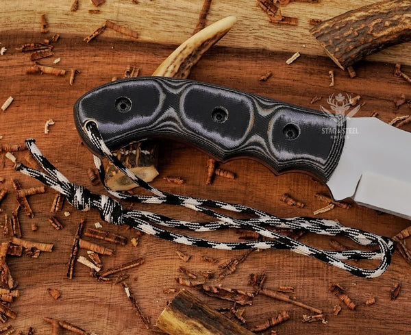 Close-up of black Micarta handle on handmade D2 tracker knife with handle pins, paracord, and full tang construction