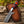 A fixed-blade bull cutter knife with a Damascus steel blade and a Pakka wood handle, resting on a brown pancake leather sheath over a weathered log with an outdoor blurred background.