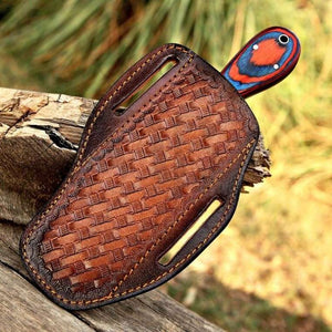 Brown leather sheath with a colorful bird head design on a wooden surface.