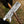 A close-up of a Damascus steel cleaver-style knife blade held upright, with a hand in a black glove gripping the wooden handle. The background is a blurred outdoor ground surface.