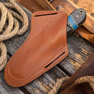 Brown leather knife sheath on a wooden surface with rope and leather background