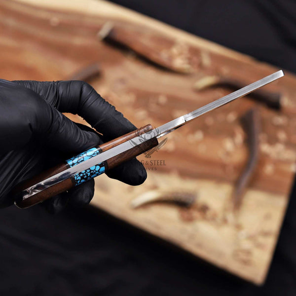 Hand holding a pocket knife with wooden handle and metal blade, against a blurred background.