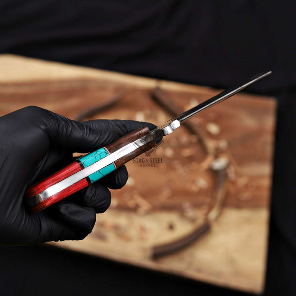 Hand holding a knife with a wooden handle and metal blade, branded 'Stag & Steel', on a wooden surface.