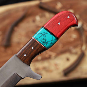 Multicolored knife handle with wooden, turquoise, and red sections on a blurred background