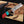 Knife with a wooden handle featuring red, turquoise, and brown colors, held by a gloved hand against a blurred background.