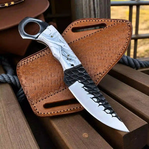 A fixed-blade knife with a white and gray marbled handle, black textured guard, and hammered blade finish, displayed diagonally on a brown leather sheath over wooden boards.