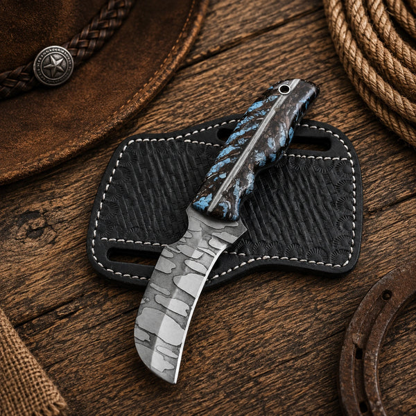 A fixed-blade knife with a patterned silver blade and a blue marbled handle, resting on a black leather sheath over a rustic wooden surface with western-themed props.