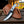 A custom fixed-blade knife with a black and silver scalloped blade and a marbled silver handle, displayed diagonally on a brown leather sheath over a wooden table.