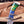 A close-up of a custom knife with a patterned Damascus steel blade and a highly polished handle featuring a gradient of blue, green, and yellow, resting on a rustic wooden surface.