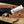 Hand holding a knife with a wooden handle and metal blade, branded 'Stag's Steel', against a workshop background.