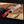 Knife with a red handle and visible brand logo held by a gloved hand on a wooden background.