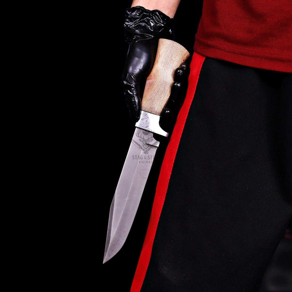 Stonewashed D2 full tang hunting knife held at the side against black background