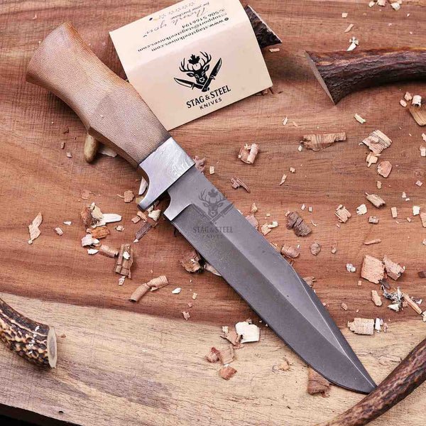 D2 full tang hunting knife with Damascus guard and lacewood handle angled on workbench