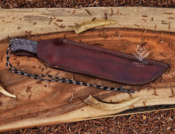 D2 steel machete knife partially fitted inside brown leather sheath with Grey Micarta handle and paracord