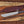 D2 steel machete knife with Grey Micarta handle, brown leather sheath, satin blade, and paracord on wood background